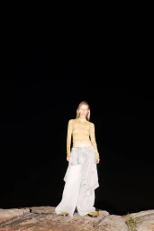Model standing on rocky terrain at night wearing a patterned top and wide light trousers for Marc Denim project.