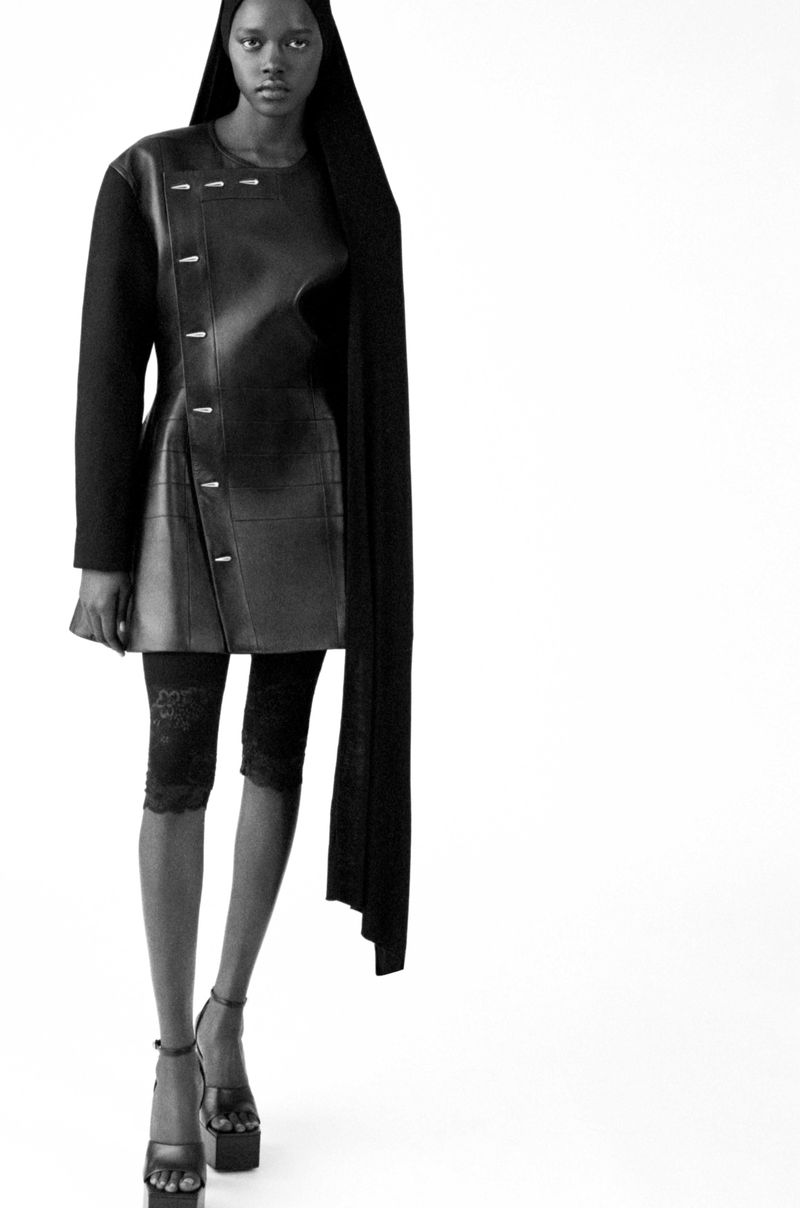 Black and white fashion shot of a slender, dark-skinned woman in a unique dress and platform sandals against a stark white background.