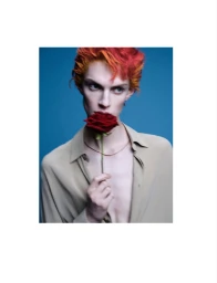 Model with red and orange hair holding a red rose in front of a blue background for Dapper Dan Magazine