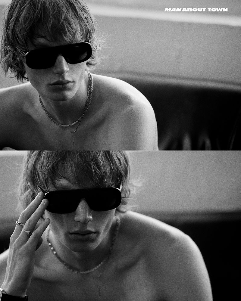 Monochrome portrait of model Calum Harper wearing sunglasses and layered silver necklaces for Man About Town.