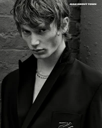 Portrait of model Calum Harper wearing a dark blazer with layered silver chain necklaces for Man About Town magazine.
