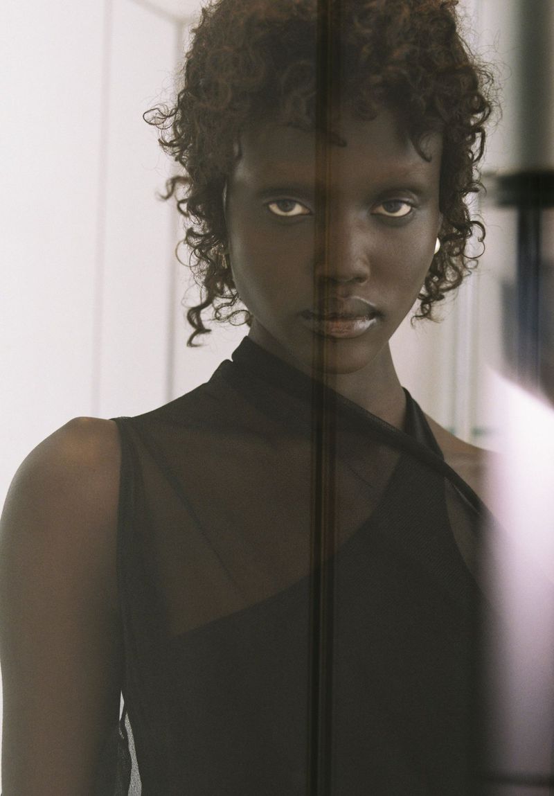 Portrait of a Black female model with curly hair wearing a black halter top posing indoors with a neutral expression and soft lighting.