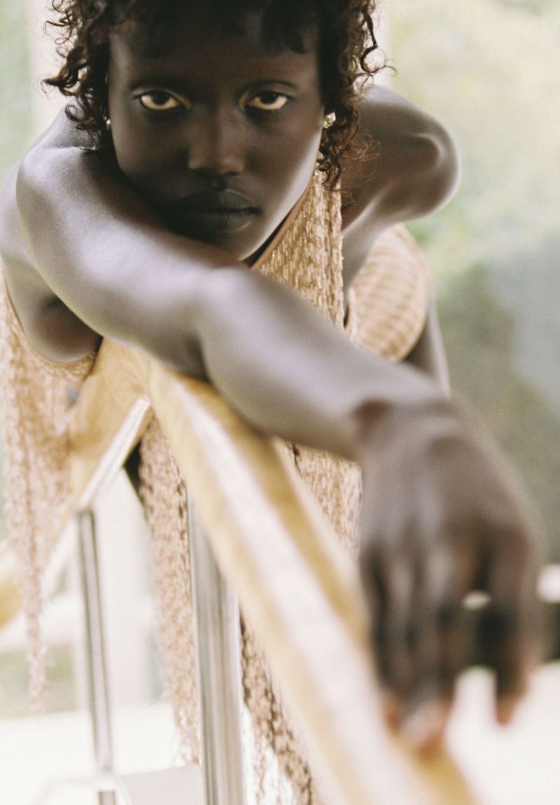 Portrait of a black woman leaning on a wooden railing, wearing a woven dress. A close-up shot with natural light, showcasing fashion and beauty.