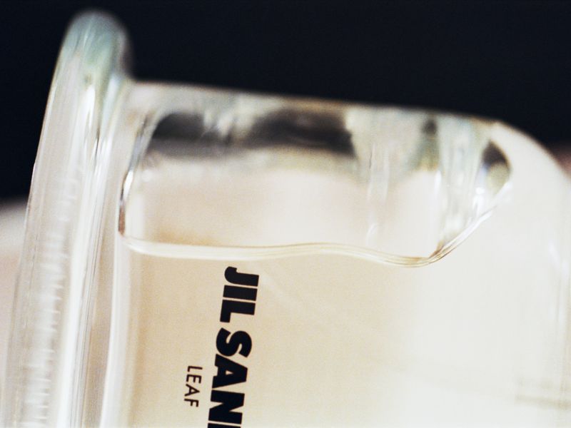 Close-up of a clear glass bottle, partially filled with a transparent liquid, featuring the text 'JIL SANDER' on its side.