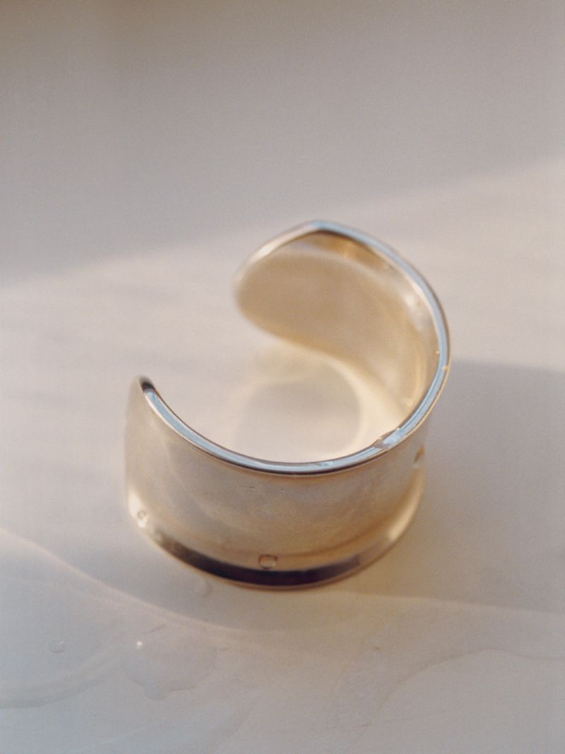 Close-up studio shot of a silver metal cuff bracelet on a white surface, showcasing its modern design and reflective texture.