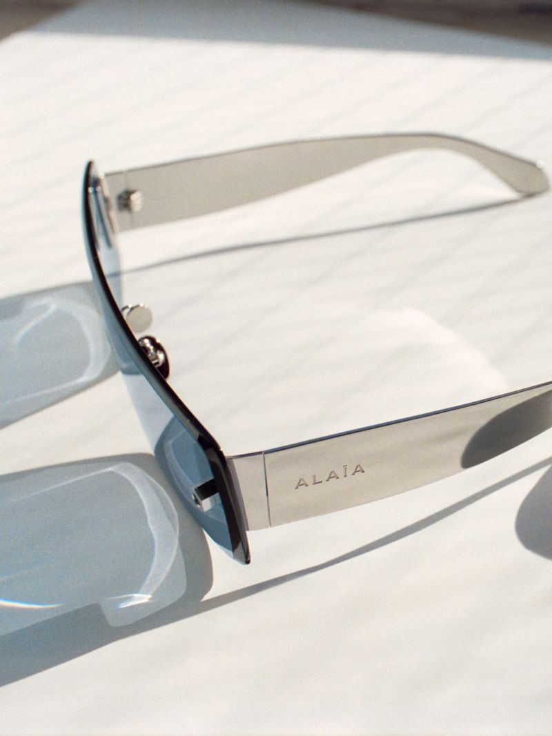 Close-up product shot of rimless blue-tinted sunglasses with metal frames, angled on a white surface in bright sunlight.