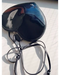 Black patent leather heart-shaped crossbody bag with long thin straps resting on a bright surface.