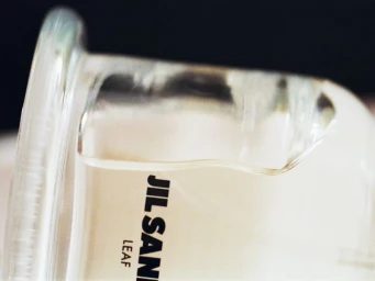Close-up of a glass jar with black Jil Sander branding against a dark background, photographed by Adam Kremer.