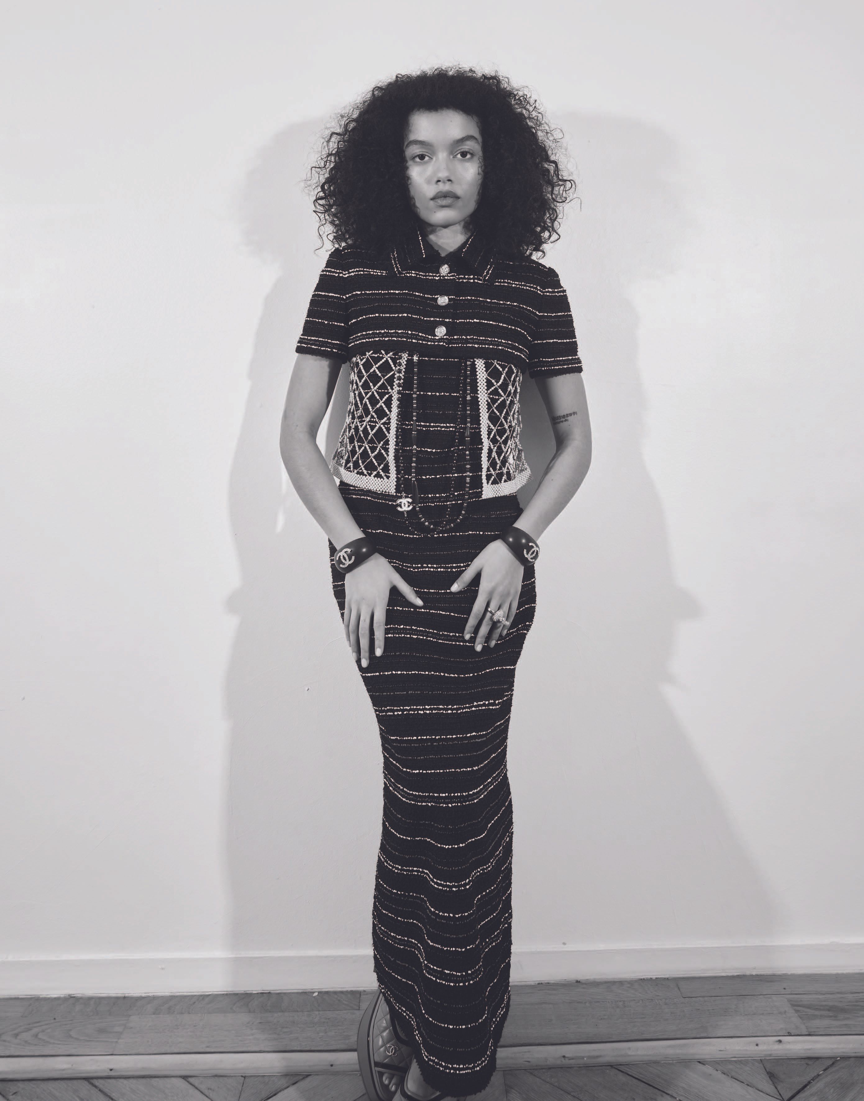 Woman in black and white striped dress and jacket, posing in front of a white wall, wearing black and white jewelry.