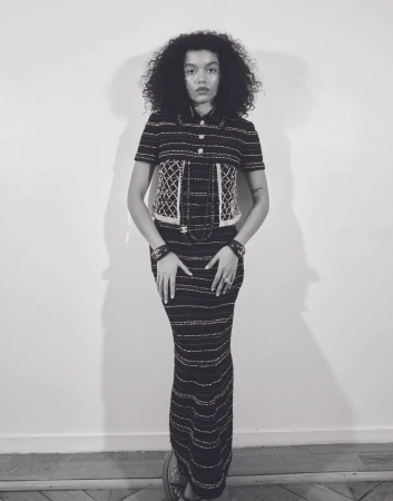 Woman in black and white striped dress and jacket, posing in front of a white wall, wearing black and white jewelry.