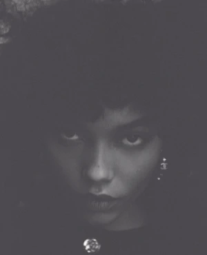 Monochrome portrait of Whitney Peak with dark curly hair and earrings against a plain background