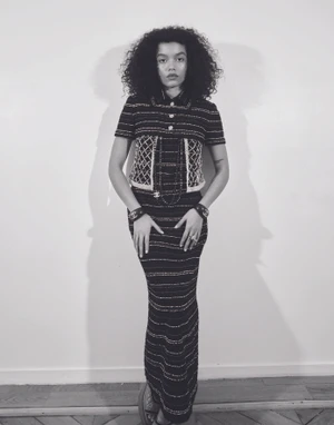 Whitney Peak wearing a dark patterned tweed matching set against a plain studio wall