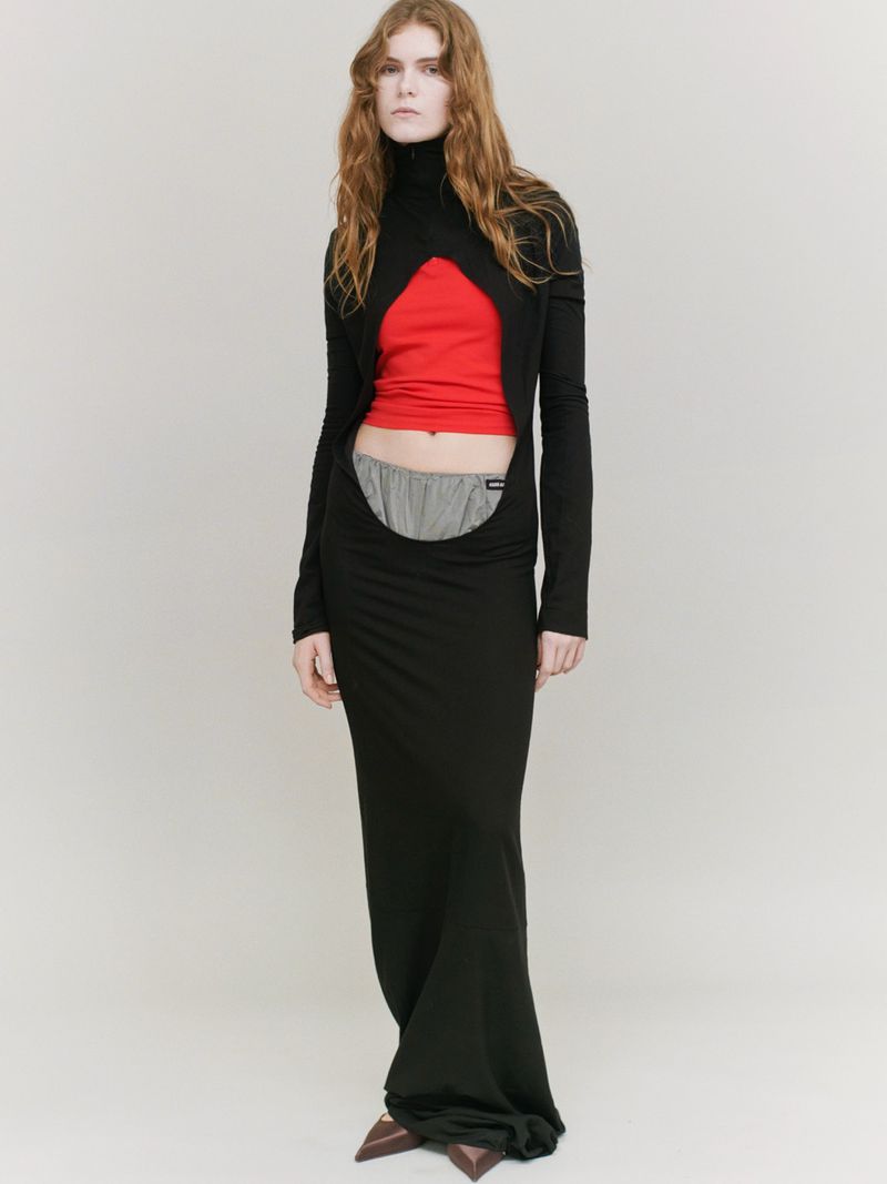 Full-length portrait of a slender woman in a black gown featuring a cut-out design, with a red top and gray shorts visible.