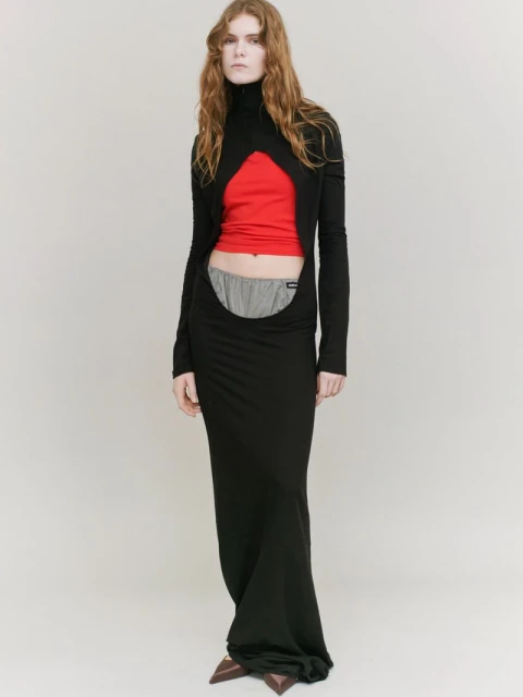 Full-length portrait of a slender woman in a black gown featuring a cut-out design, with a red top and gray shorts visible.