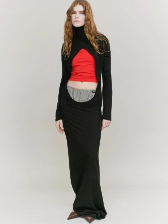 Full-length portrait of a slender woman in a black gown featuring a cut-out design, with a red top and gray shorts visible.