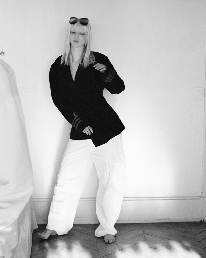 Model Vilma Friedlander wearing dark jacket and white trousers poses against a plain wall for D Repubblica