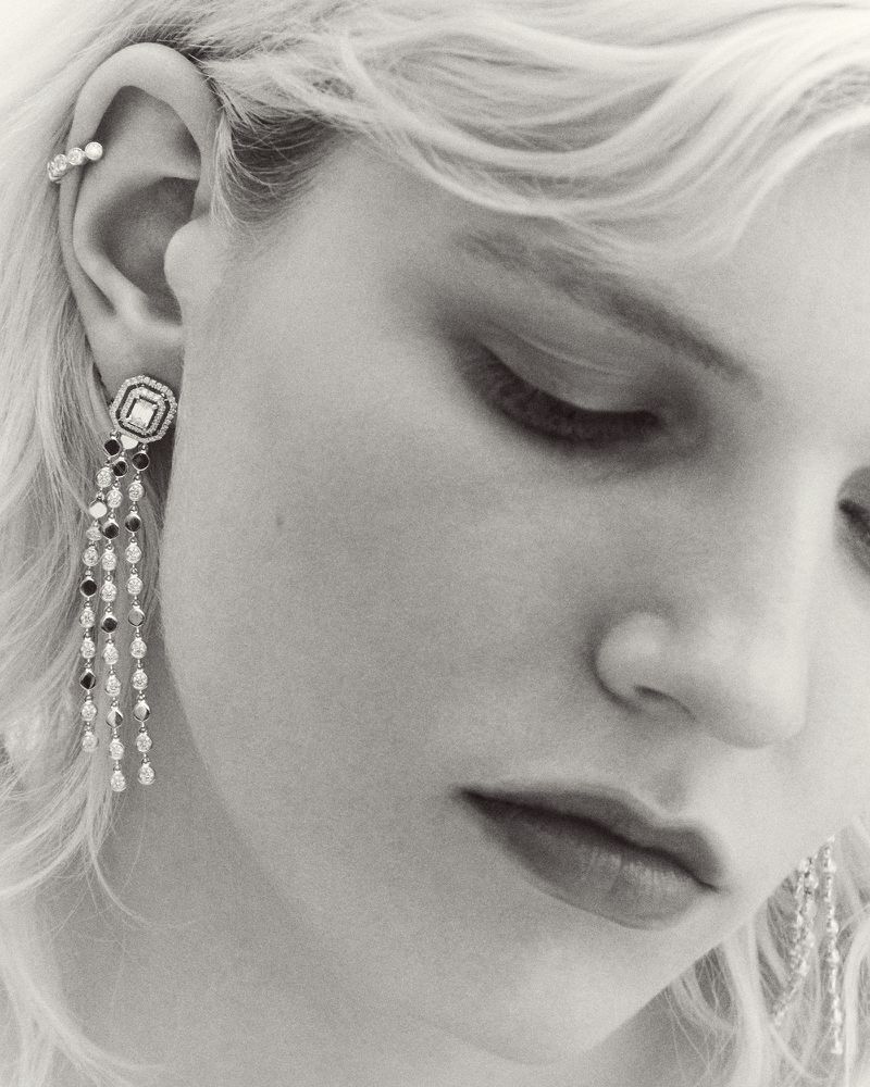 Close-up monochrome portrait of a woman wearing ornate crystal drop earrings and an ear cuff, photographed by Florent Tanet.