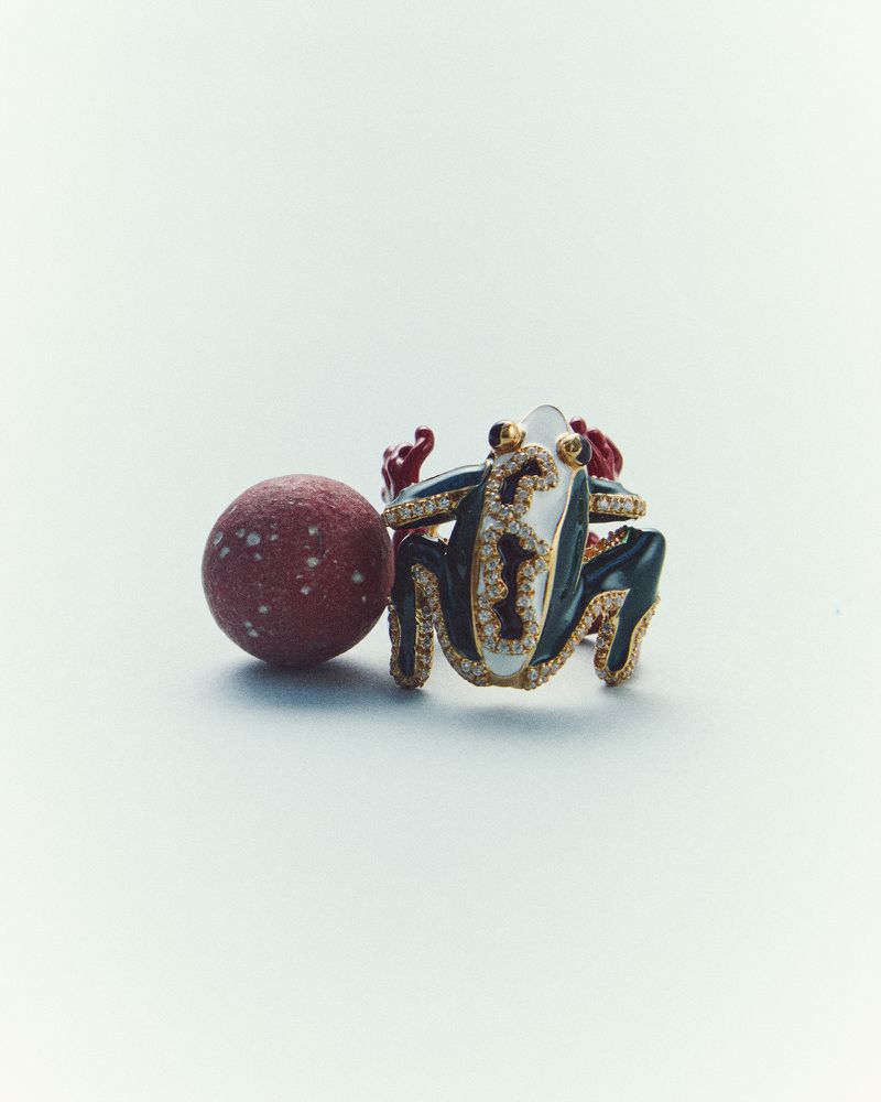 Jeweled frog sculpture with gemstone-studded green and white enamel and a textured red ball, creating an eye-catching display.