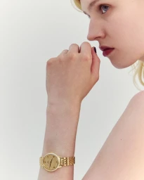 Close-up portrait of a woman wearing a gold watch on her wrist, shot against a plain white background for the CAMILLE project by Beyond Noise.