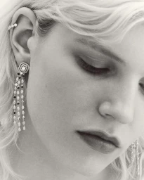 Close-up monochrome portrait of a woman wearing ornate crystal drop earrings and an ear cuff, photographed by Florent Tanet.