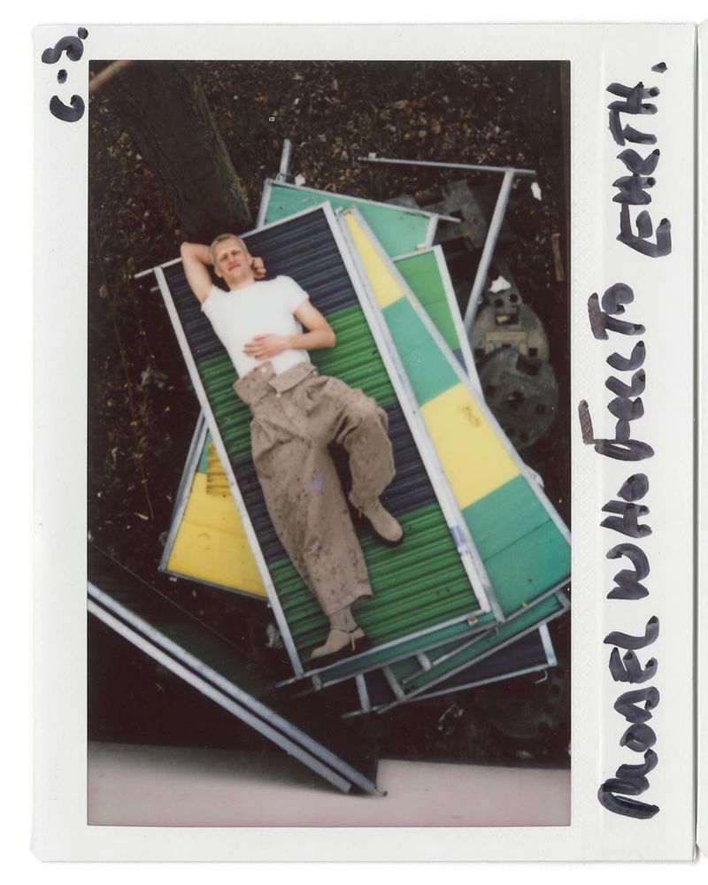 Overhead shot of a fair-skinned man reclining on a pile of colorful platforms outdoors surrounded by trees and dark foliage.