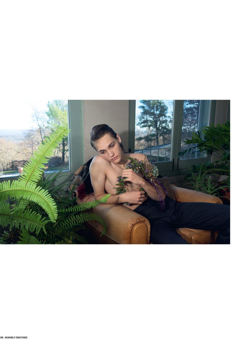 Young adult relaxing in a brown leather chair near a window, surrounded by lush green plants and holding flowers in an indoor environment.