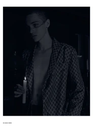 Model holding a lit candle wearing an unbuttoned patterned jacket in a dark moody editorial portrait