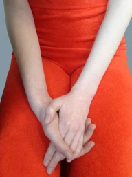 Close-up of a person wearing a bright red textured top and trousers, with hands clasped together in the lap.
