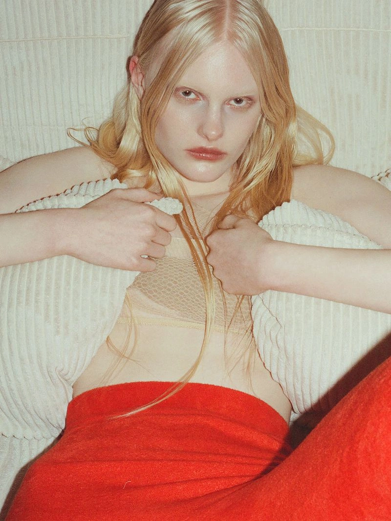 Portrait of a blonde model holding textured white pillows against a neutral backdrop, photographed by Yulia Plakhotnikova for Hi-rez.