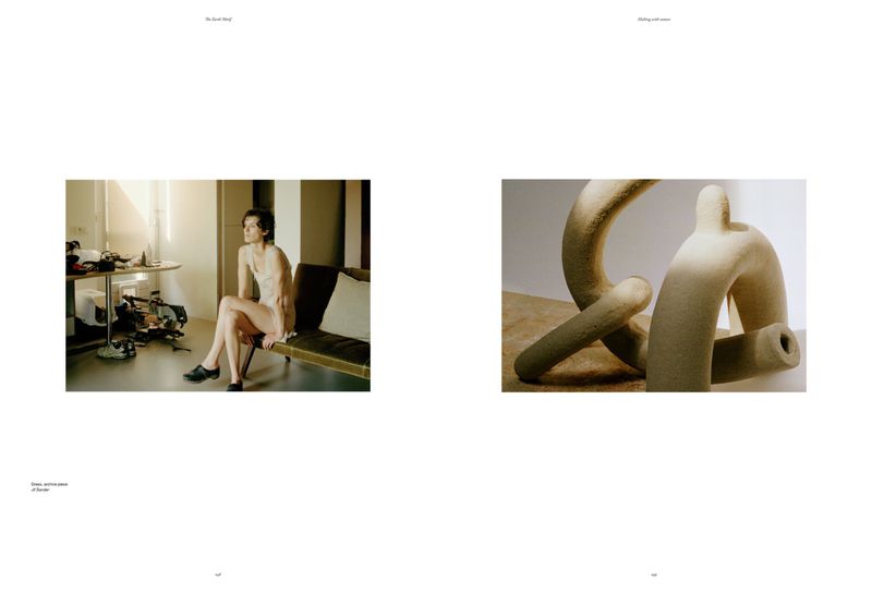 Indoor scene with a woman sitting on a stool, wearing a light-colored top, with an abstract sculpture visible, captured with natural light.