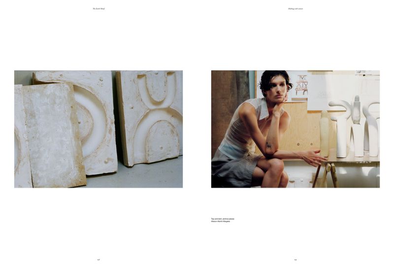 Woman in sleeveless top sits with plaster casts of objects in indoor studio setting; muted color palette, editorial aesthetic.
