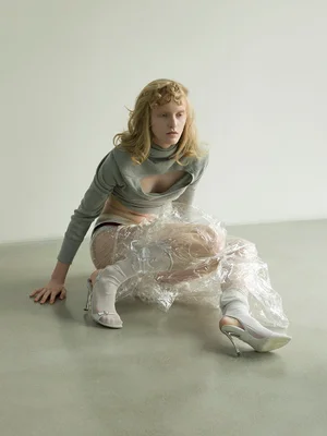 Model seated on the floor wearing a grey cut-out top and translucent plastic wrap wrapped around the lower body.