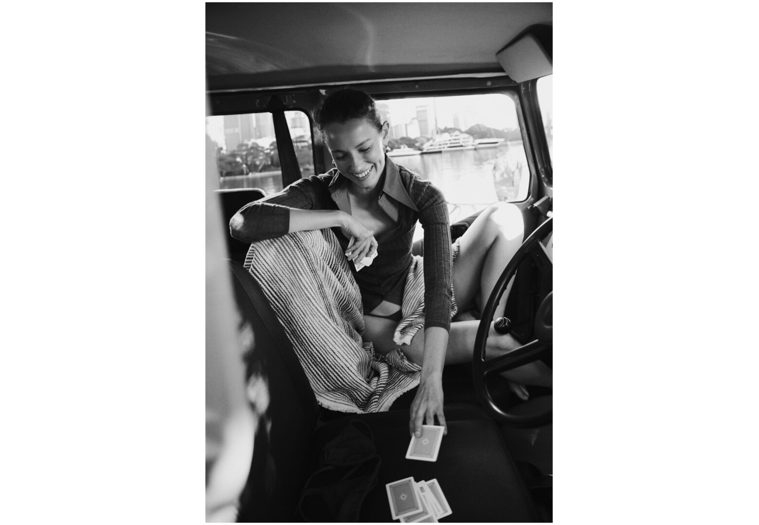 Monochrome image of a smiling woman seated inside a car holding playing cards, captured by Dan Roberts for Side-note.