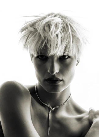 Portrait of a woman with platinum blonde hair wearing a snake necklace against a bright background in a monochrome photograph.