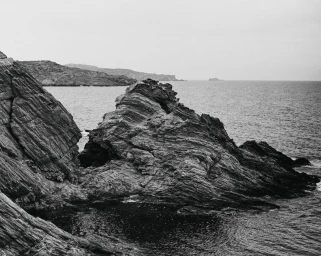 Monochrome landscape photograph of jagged rocky cliffs meeting the dark open ocean under an overcast sky.