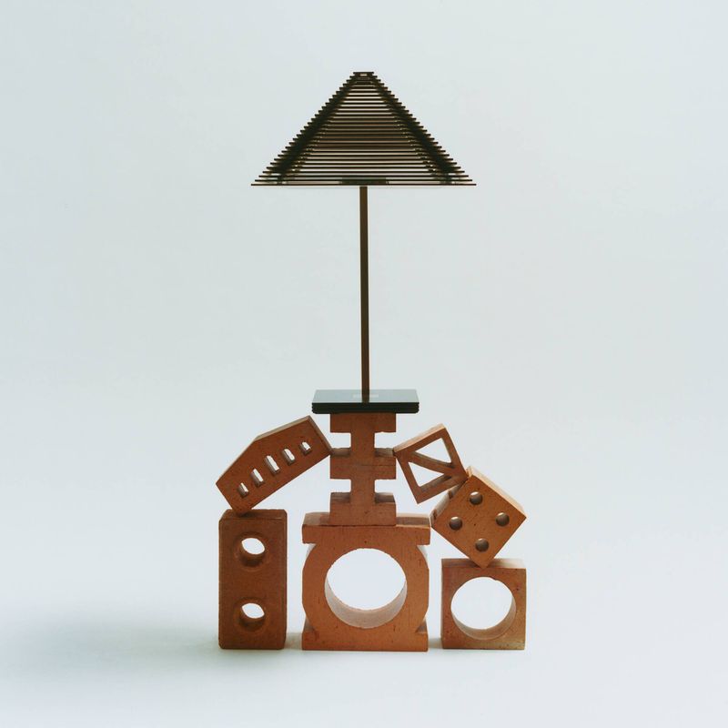 Abstract art installation with geometric shapes including bricks, cubes, triangles, and pyramid structure on a clean white background.
