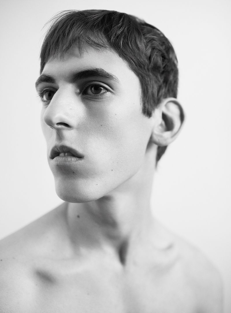 Monochrome portrait of a fair-skinned young adult male with short brown hair, looking off-camera in a photo studio setting with soft lighting.