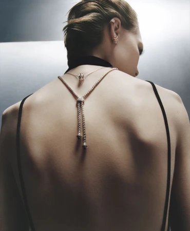 Model seen from behind wearing a black evening dress and layered fine jewellery against a grey background.