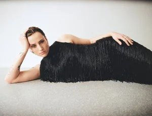 Model lying on a textured grey surface wearing a black fringed dress for L'Officiel Austria