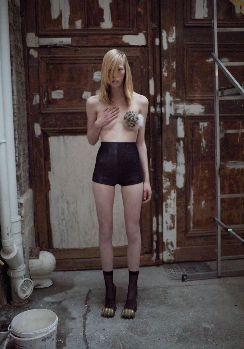 Model standing in front of large weathered wooden doors wearing dark high-waisted shorts and sheer black socks