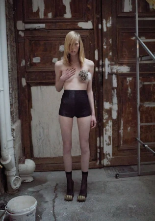Model standing in front of large weathered wooden doors wearing dark high-waisted shorts and sheer black socks