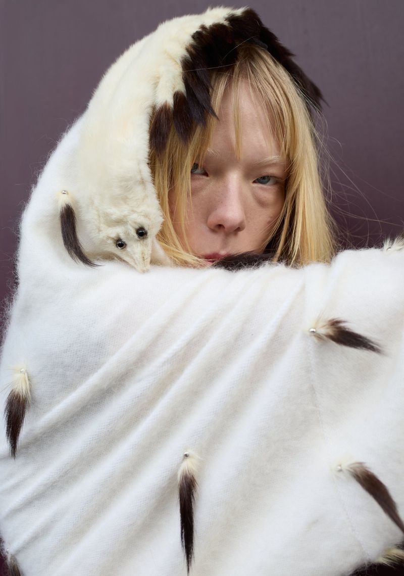 Adult female with pale complexion wearing a white fur-like shawl and a stoat draped over her head in a studio shot.