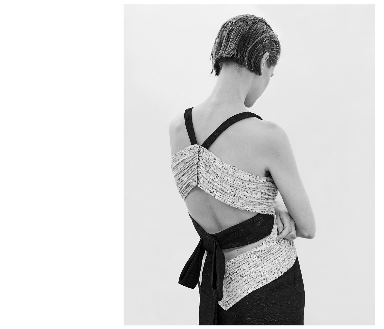 Back view of a model in a monochrome shot wearing a textured dress with a bow. Fashion photography in an indoor setting.