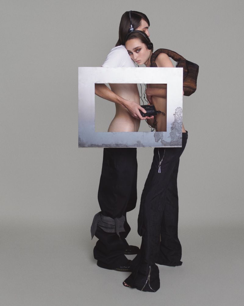 Two people pose in a studio with a square frame obscuring their bodies. One person wears headphones and holds a music player.