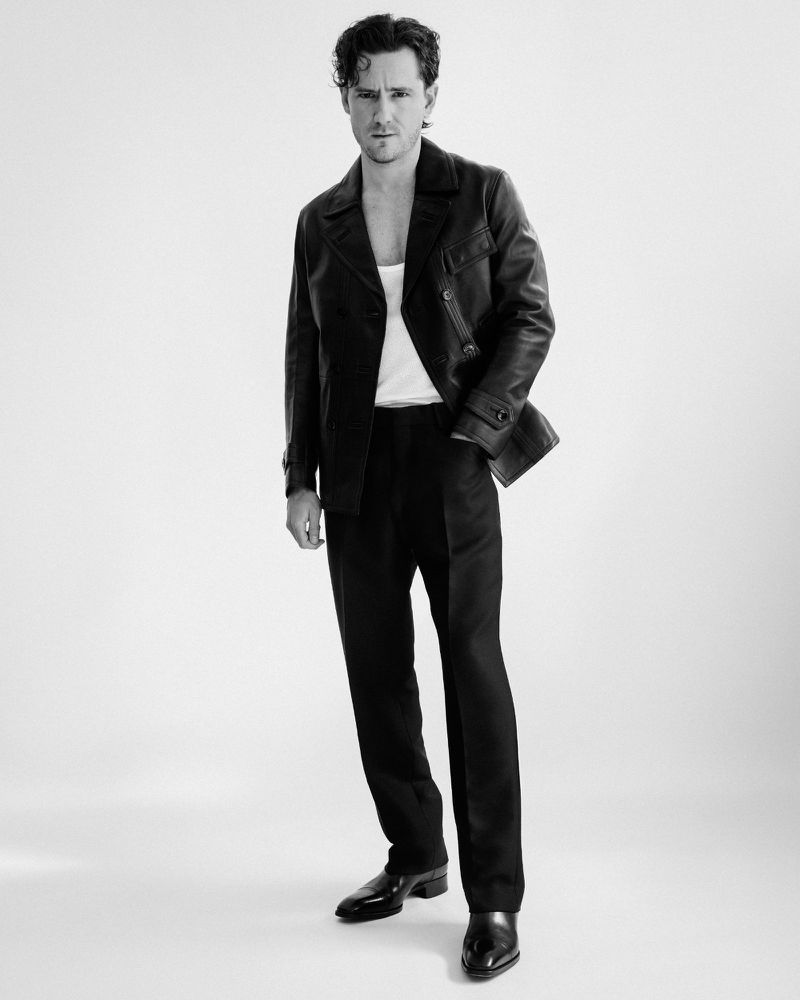 Actor Lewis Pullman wearing a dark leather jacket over a white tank top against a white seamless studio background.