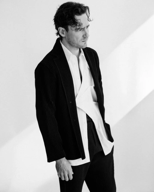Monochrome portrait of a man in a white shirt and black jacket looking off-camera against a bright, neutral background with soft lighting.
