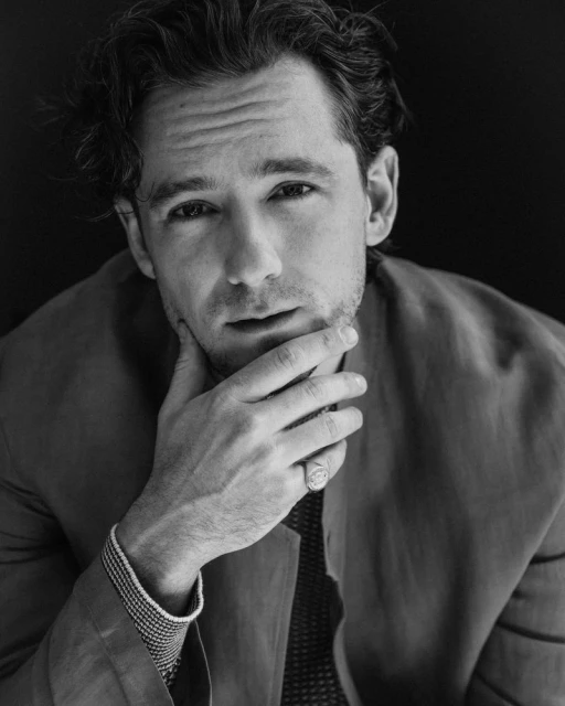Black and white portrait of an adult male with dark hair, wearing a jacket and shirt, with his hand near his chin.