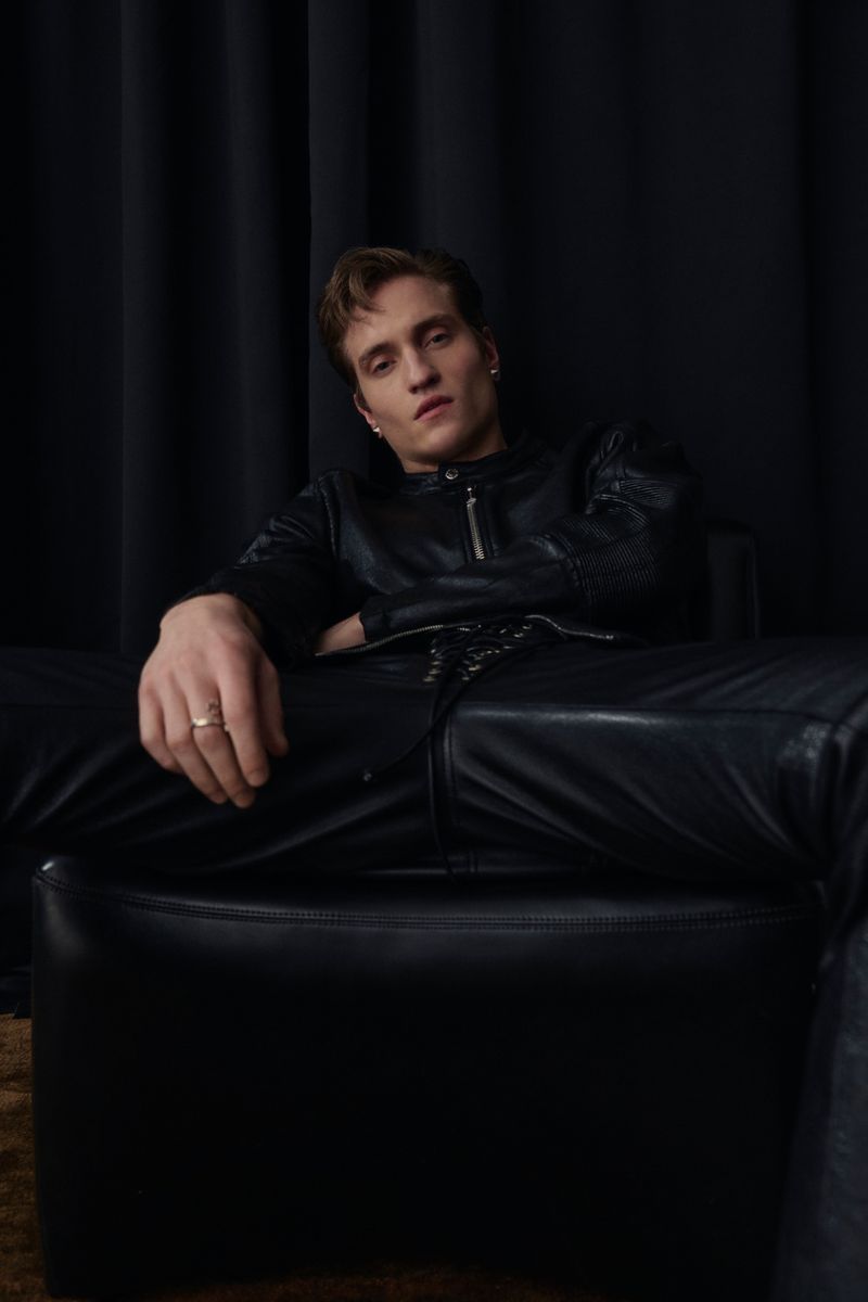 Portrait of an adult male sitting in a black leather chair against a dark backdrop in an indoor setting with studio lighting.