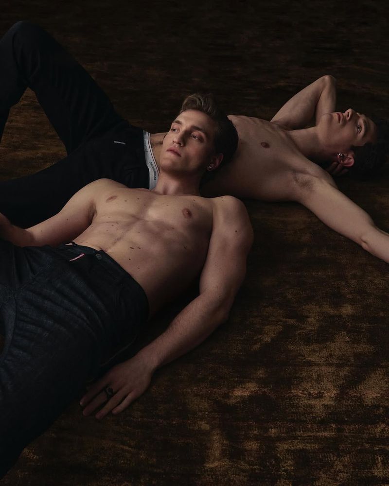 Two shirtless male models lying on a dark textured floor for Man About Town magazine