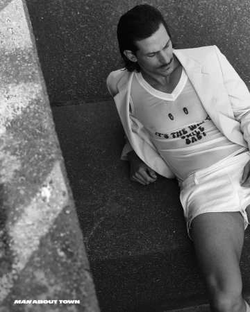 Man wearing a blazer and graphic tank top reclining outdoors on concrete steps in a monochrome editorial photograph